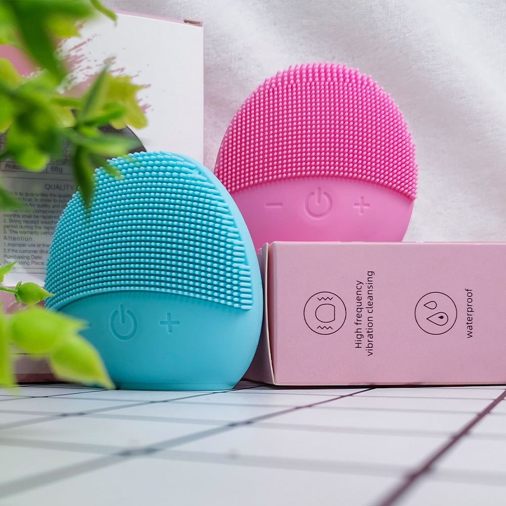 Rechargeable facial cleansing brush in blue and pink colors next to packaging, showcasing waterproof design and vibration technology.